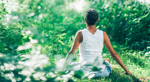 Back view of woman sitting in forest with arms extended at side